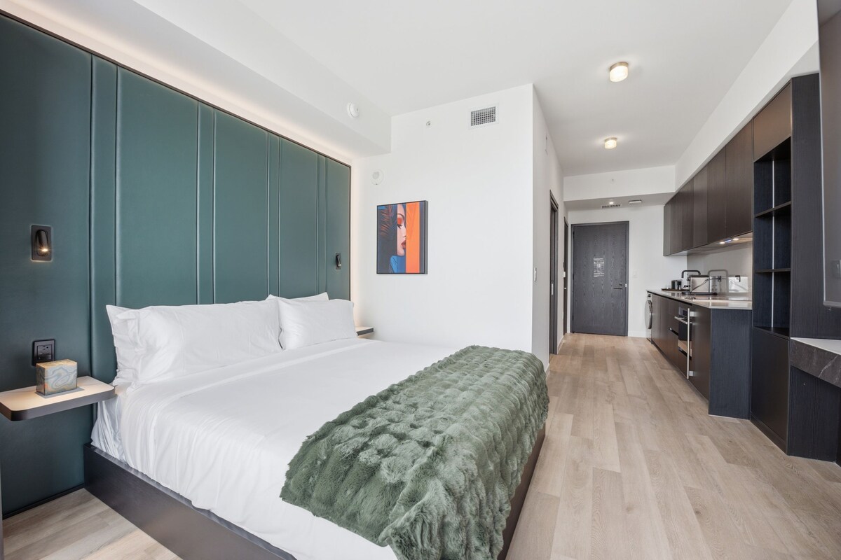 A modern bedroom with a large bed, a green throw blanket, and a nightstand with a lamp.