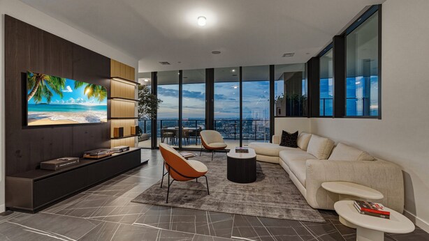 Una sala de estar moderna con un televisor grande, un sofá, dos sillones, una mesa de centro y vistas de la ciudad.