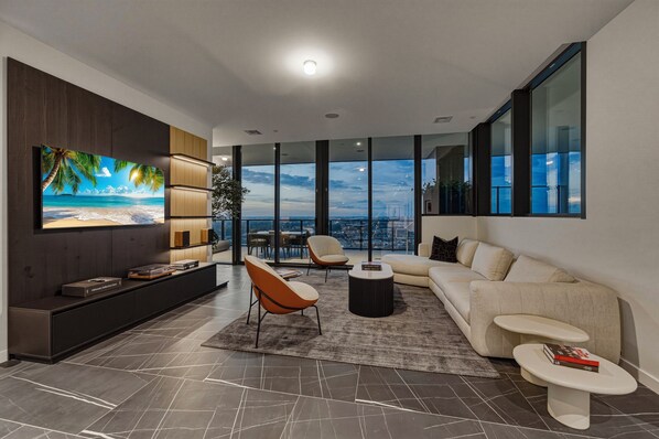 A modern living room with a large TV, a sofa, two armchairs, a coffee table, and a view of the city. - E11EVEN Presidential Penthouses (Miami)
