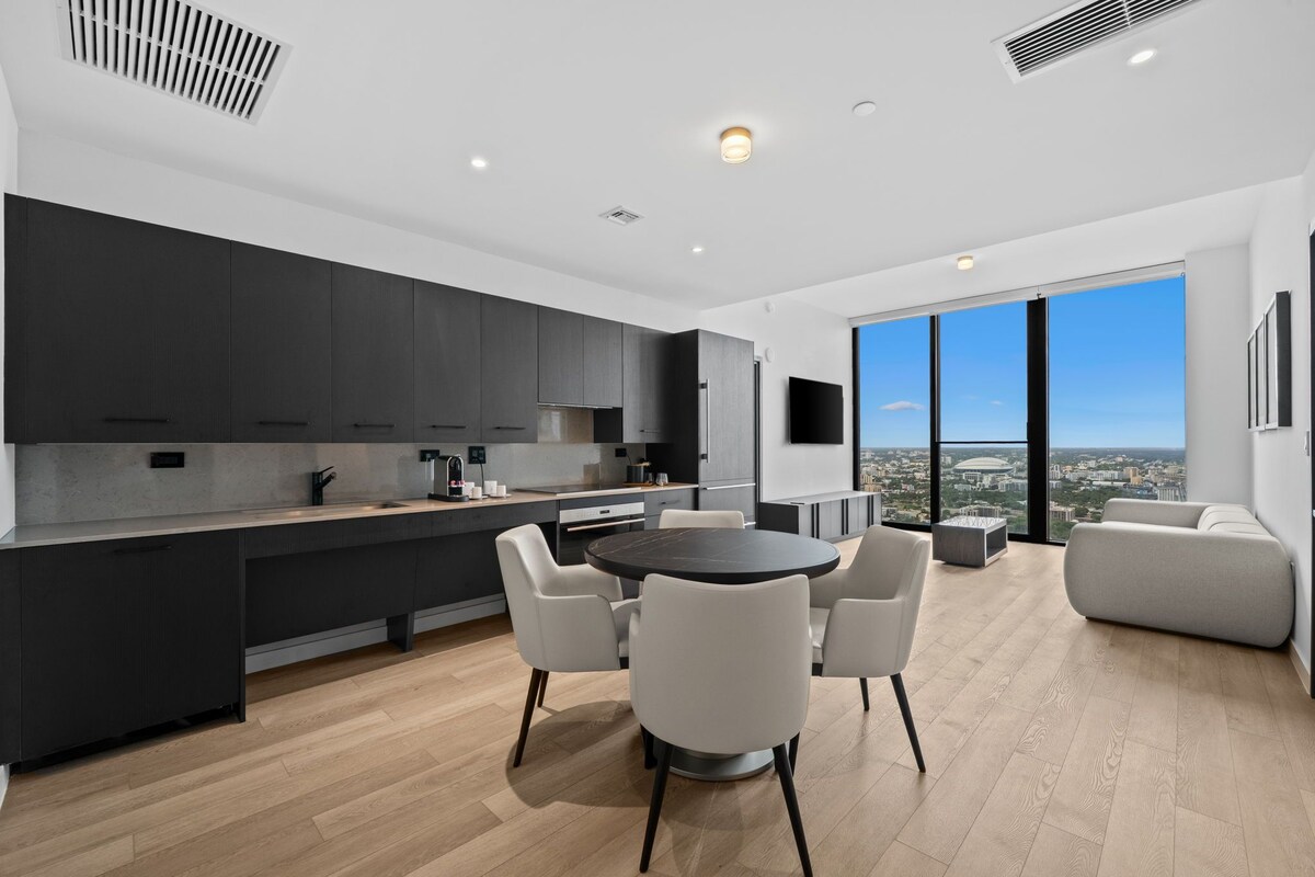 A modern kitchen with dark cabinetry, a central island, and a dining area with a round table and chairs.