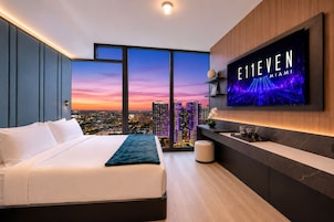 A modern hotel room with a large bed, a TV mounted on the wall, and a city view.
