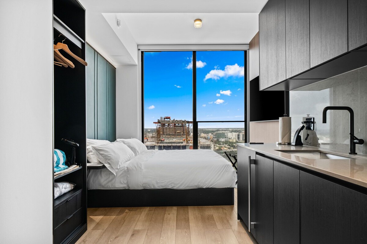 A modern bedroom with a large bed, a wardrobe, and a view of a cityscape through a large window.