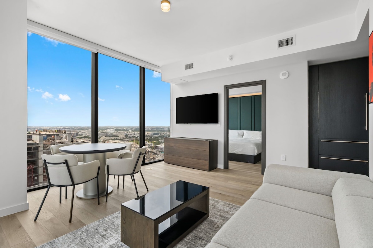 A modern living room with a large window, a round table, a sofa, and a flat-screen TV.
