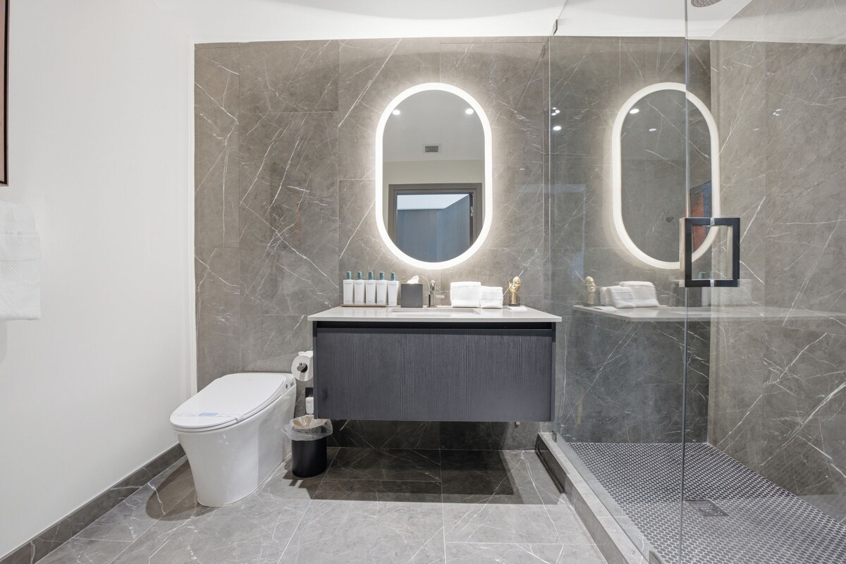 A modern bathroom with a marble vanity, a toilet, and a glass shower enclosure.