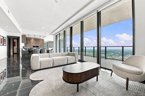 Un salon moderne avec un grand canapé, une table basse et une vue sur la ville grâce à de grandes fenêtres.