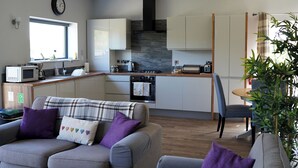 Eine moderne Küche mit Mikrowelle, Toaster und Herd, ein Essbereich mit Tisch und Stühlen sowie ein Wohnzimmer mit Sofa und Kissen.