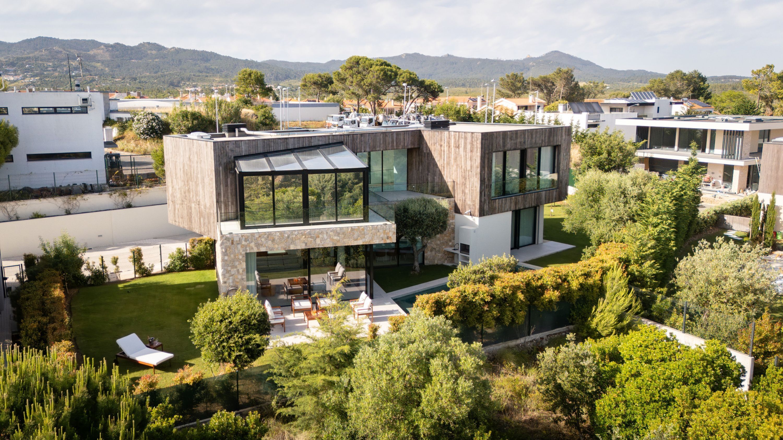 Een modern huis met een glazen serre, een zwembad en een verzorgde tuin.