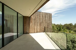 En moderne balkon med glasgelændere, en trævæg og udsigt til grøn natur.
