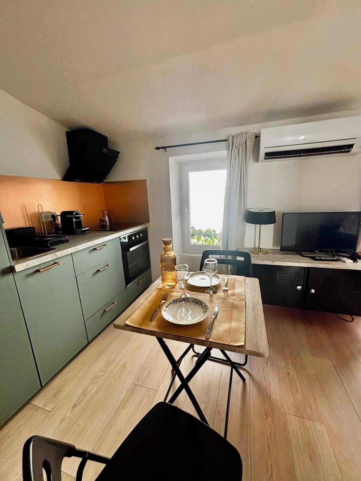 Een compacte keuken met een eettafel voor twee personen, een televisie en een airconditioner.