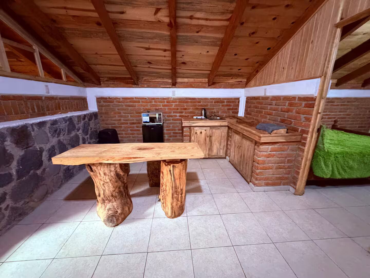 Une cuisine rustique avec une table et des placards en bois, un mur en pierre et un sol carrelé.