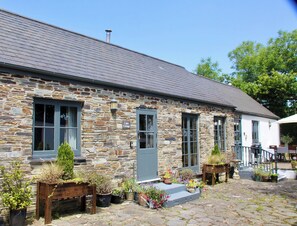 A stone cottage with a tiled roof, a wooden bench, and potted plants. - Cider Cottage (Launceston)