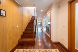Eine Holztreppe führt zu einer zweiten Etage, einem Flur mit einem gemusterten Teppich und einem großen Fenster mit Ausblick.