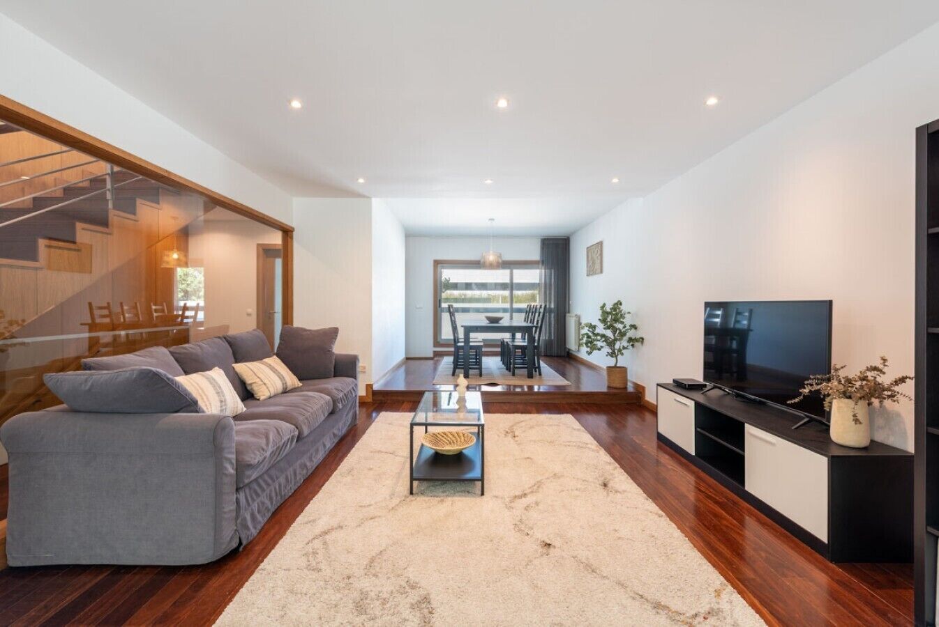 A modern living room with a sofa, coffee table, TV, and a staircase leading to another level.