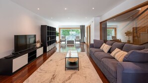 Ein modernes Wohnzimmer mit Flachbildfernseher, Bücherregal, Sofa und Treppe.