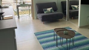 Ein modernes Wohnzimmer mit einer Couch, einem Couchtisch und einem Fernseher. Ein Balkon bietet Blick auf Gebäude.