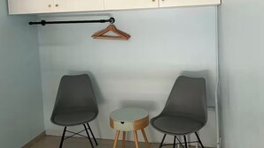 Ein Zimmer mit einem weißen Kleiderschrank, zwei grauen Stühlen, einem kleinen runden Tisch und einer Pendelleuchte.