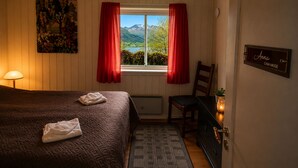 A bedroom with a bed, a chair, a window with curtains, a lamp, a painting, and a sign on the wall.