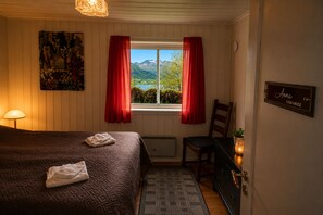 A bedroom with a bed, a chair, a window with curtains, a lamp, a painting, and a sign on the wall.