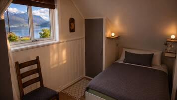 Een slaapkamer met een bed, een stoel, een raam met uitzicht op bergen en een wandplank met een lamp.
