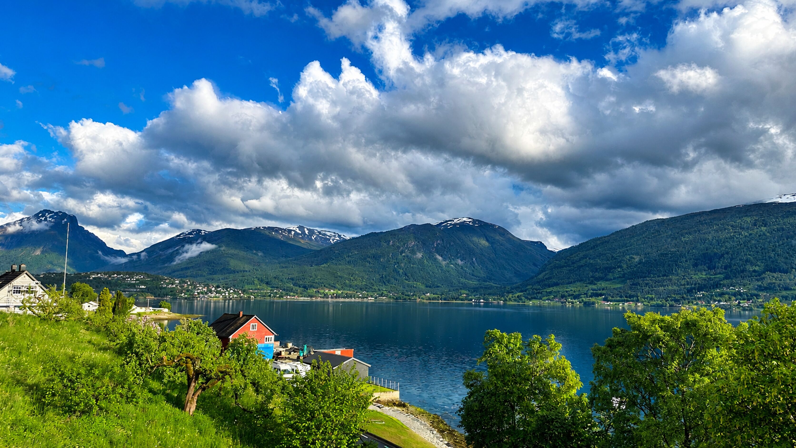 Vista de un lago con montañas, una casa y un muelle.