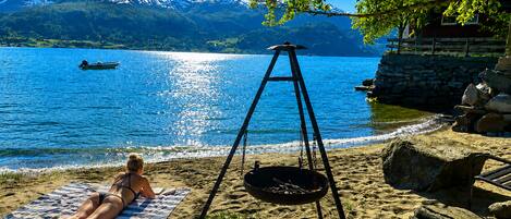 A beach with a person sunbathing, a swing, and a boat on the water.