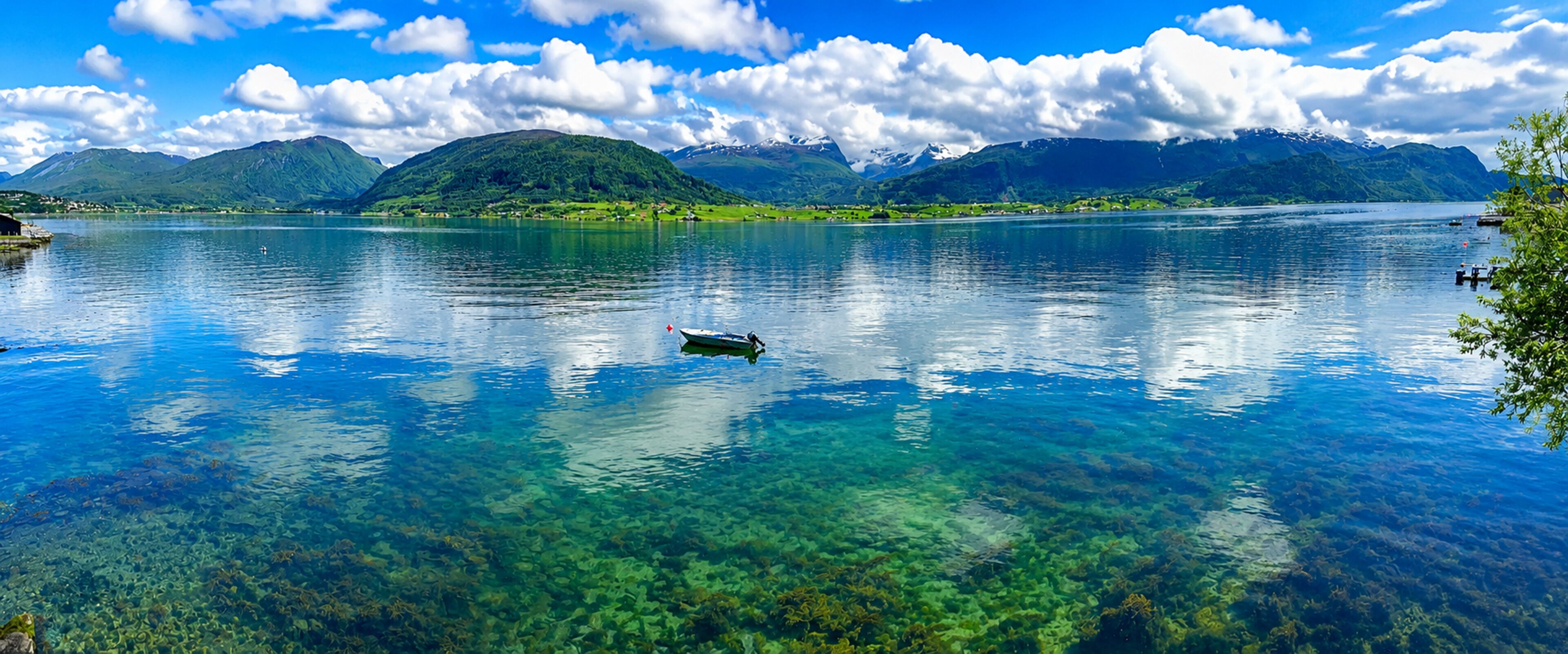 A clear lake with a boat, mountains in the background, and clear water.