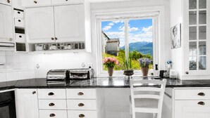 A kitchen with white cabinets, a black countertop, a window with a view of mountains, and a chair.