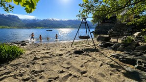 A sandy beach with a swing set, a stone building, and mountains in the background.
