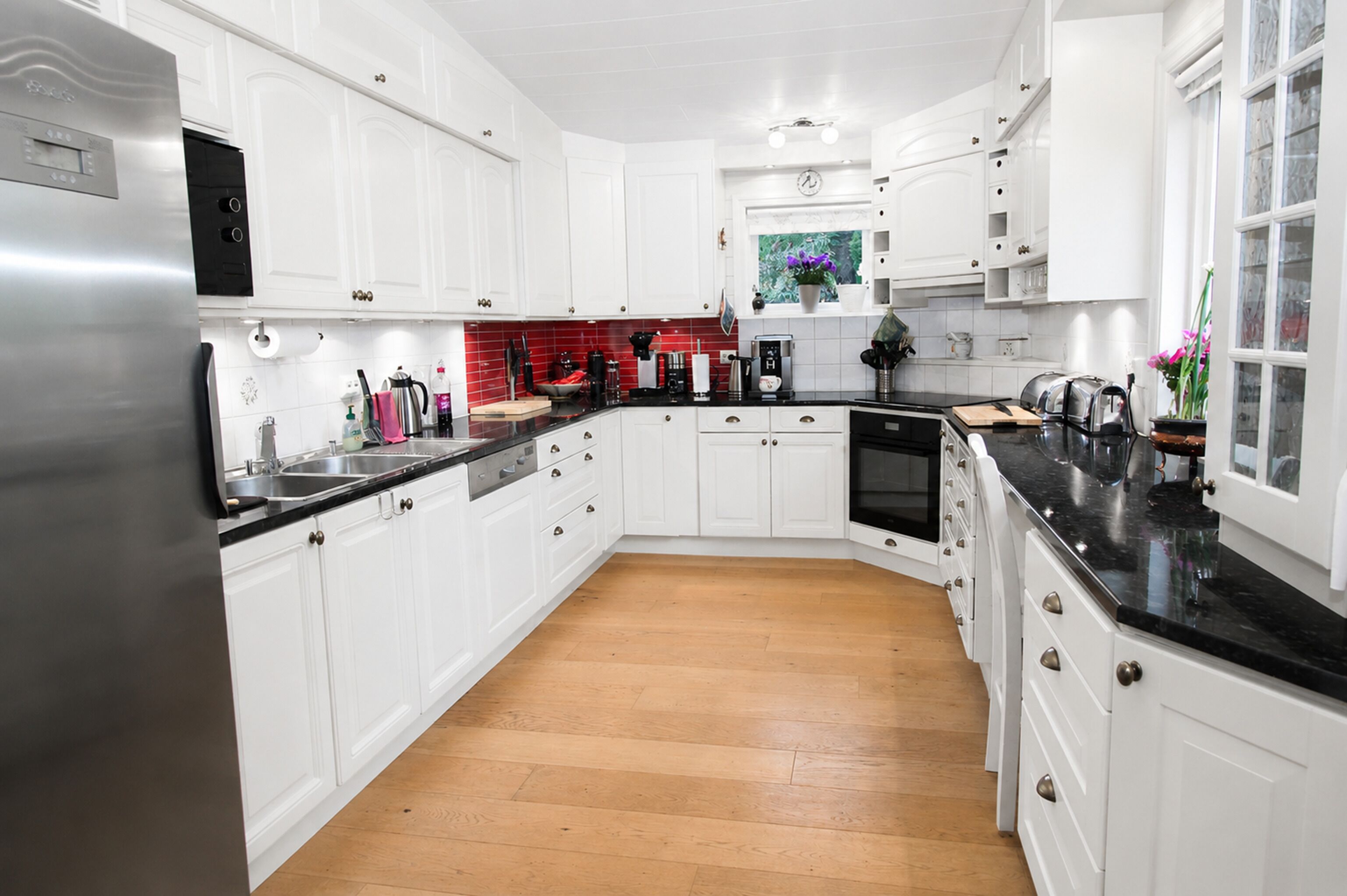 Una cocina moderna con armarios blancos, un refrigerador de acero inoxidable, una encimera negra y piso de madera.
