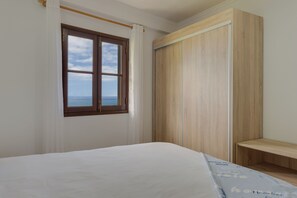 A bedroom with a bed, a window with a view, and a wooden wardrobe. - Maiata Beach 3 (Madeira)
