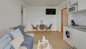 A modern living room with a sofa, a dining area with chairs, a TV mounted on the wall, and a washing machine in the corner. - Maiata Beach 3 (Madeira)