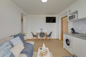 A modern living room with a sofa, a dining area with chairs, a TV mounted on the wall, and a washing machine in the corner. - Maiata Beach 3 (Madeira)