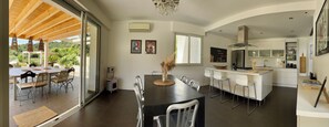 A modern kitchen with a built-in oven, a dining area with a large table and chairs, and a view of a lush garden through a sliding glass door. - VillaSerenita Heated Pool, Jacuzzi, Ping Pong (ALATA)