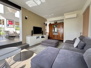 Ein modernes Wohnzimmer mit grauem Sofa, einem Flachbildfernseher, einer weißen Unterhaltungsanlage und einem Holzschrank.
