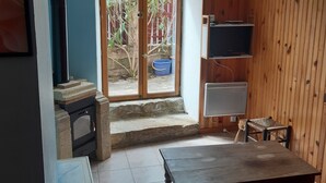 Ein Zimmer mit Kamin aus Stein, einem Holztisch, einem roten Bett, einem Fernseher und Blick auf einen Garten durch eine Glastür.