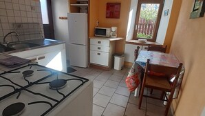 Eine kompakte Küche mit Gasherd, Mikrowelle und Kühlschrank. Ein kleiner Essbereich mit Tisch und Stühlen ist ebenfalls vorhanden.