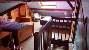 Ein Schlafzimmer im Loft-Stil mit einem hölzernen Bett, einem Sessel, einem kleinen Tisch und einem Fenster.