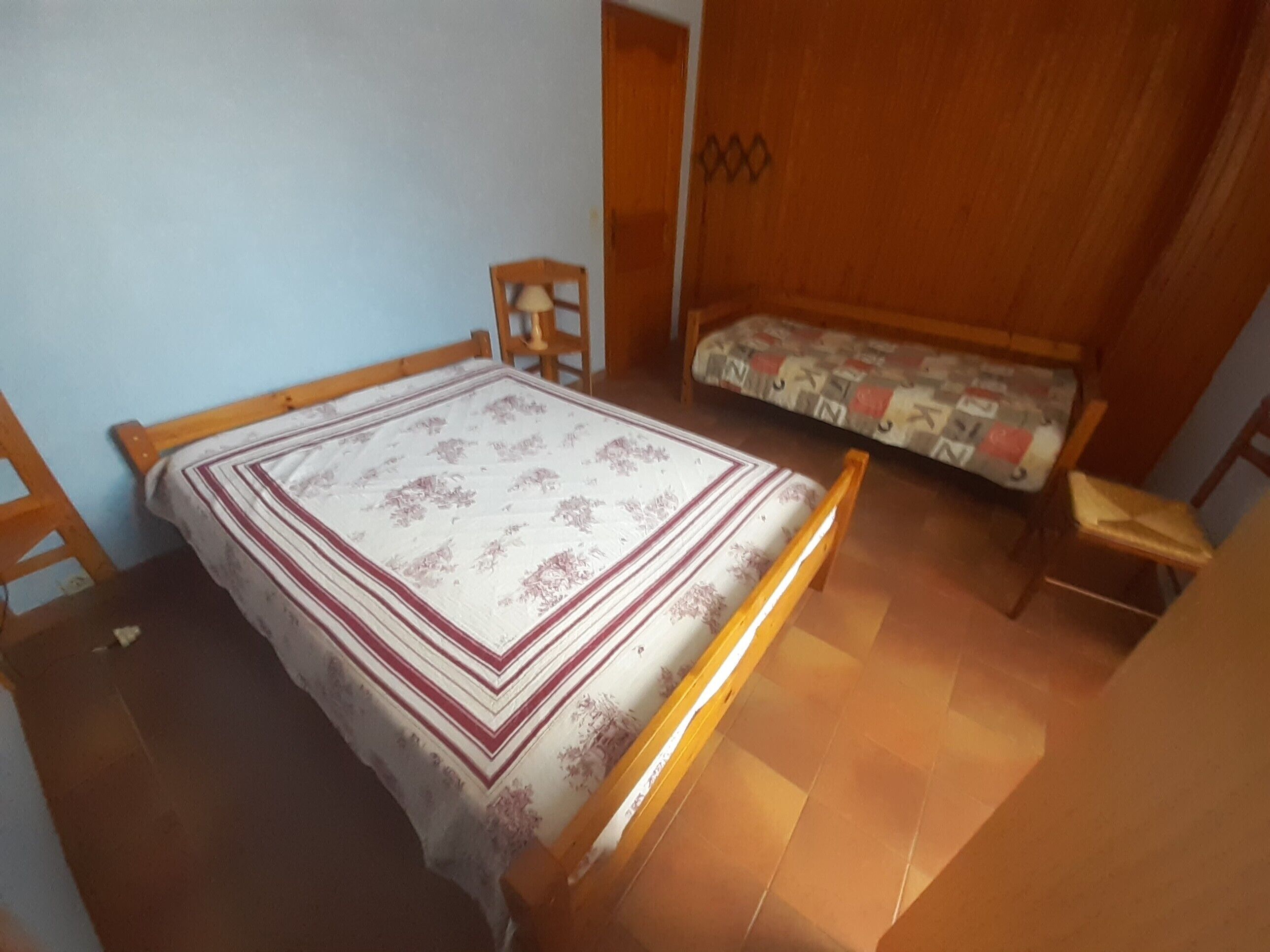 Een kamer met een bed, een houten stoel, een bank en een kledingkast van hout.