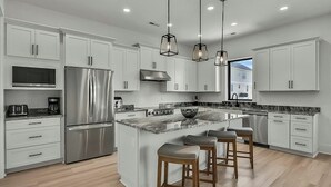 A modern kitchen with white cabinets, a stainless steel refrigerator, a large island with bar stools, and pendant lighting. - Sleeps 28-Blue Whale-Pool-12 Bedrooms & 4 Kitchens (North Myrtle Beach)