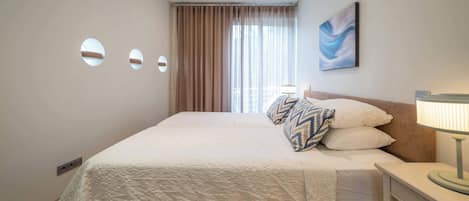 Habitación de hotel con cama, mesita de noche, lámpara, un cuadro y ventana con cortinas.