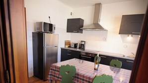 Une cuisine compacte équipée d’un réfrigérateur, d’un four à micro-ondes et d’une cuisinière. On y trouve une table à manger avec des chaises et une bouteille de vin.