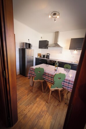 A compact kitchen with a refrigerator, microwave, and stove. There is a dining table with chairs and a bottle of wine. - Vacation Rental in the Old Wine Cellar, ideally located in Central Alsace (Epfig)