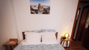 Un lit avec une couvre-lit à motifs, des oreillers, une table de chevet avec une lampe et un tableau encadré au mur.