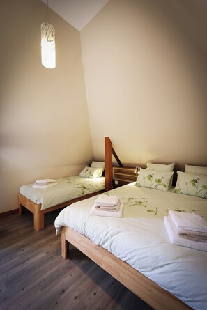 A bedroom with two single beds, a wooden headboard, a hanging light fixture, and a wooden floor. - Vacation Rental in the Winemaker's Attic, ideally located in Central Alsace (Epfig)