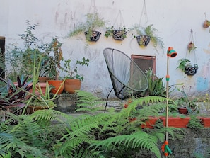 A garden with various potted plants, a chair, and a water feature. - Quintal Oceano (Rio de Janeiro)