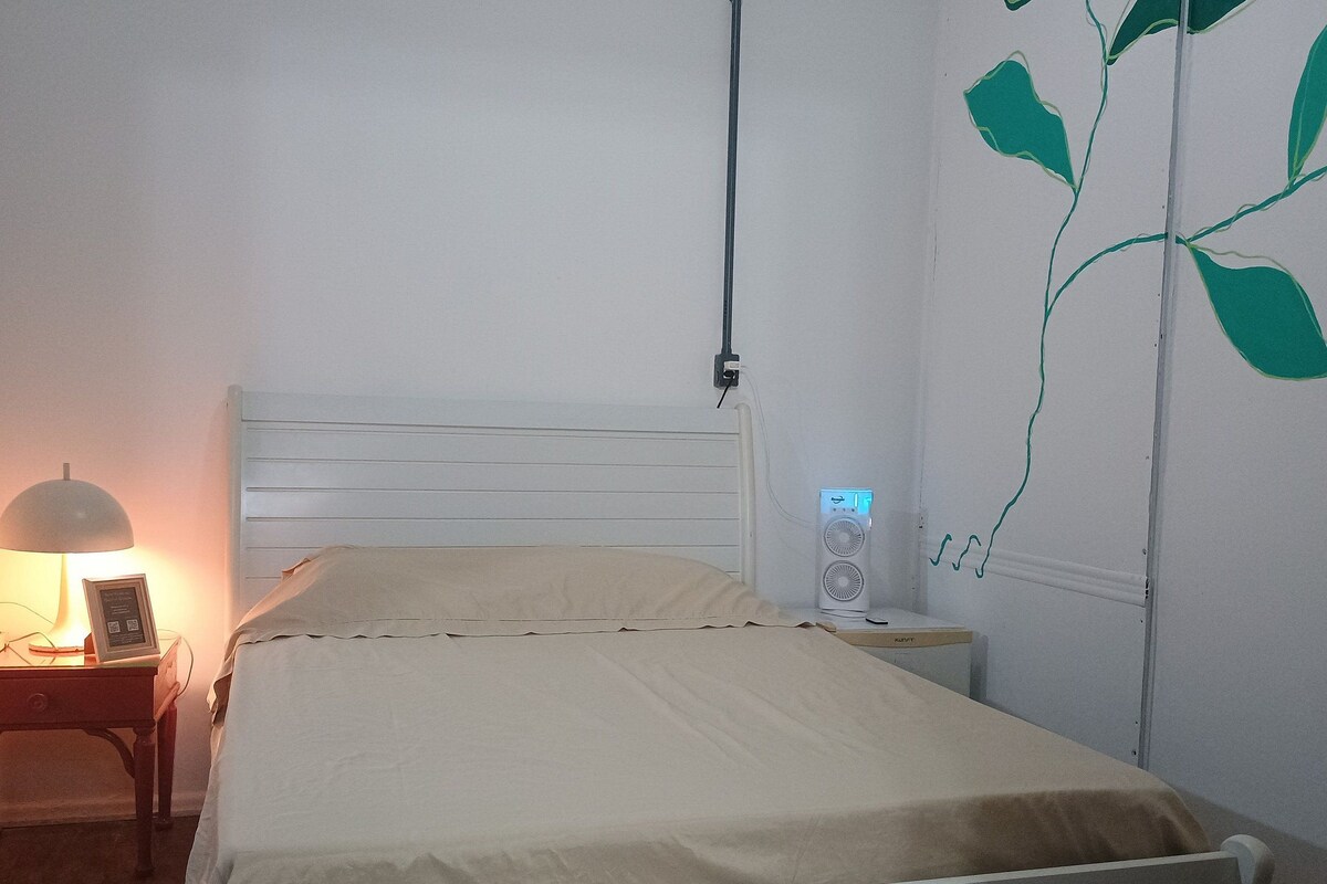 A bed with a white headboard, a bedside table with a lamp, and a wall-mounted speaker.