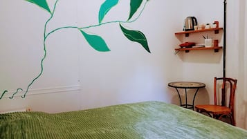 Quarto com cama, cadeira, mesa pequena e parede com padrão de folha verde.