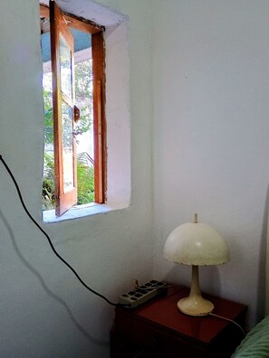 A room with a window, a lamp on a bedside table, and a power outlet.