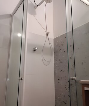 Una ducha con mampara de vidrio y ducha de mano.
