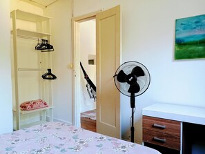 A bedroom with a bed, a fan, a wooden dresser, and a closet with shelves.